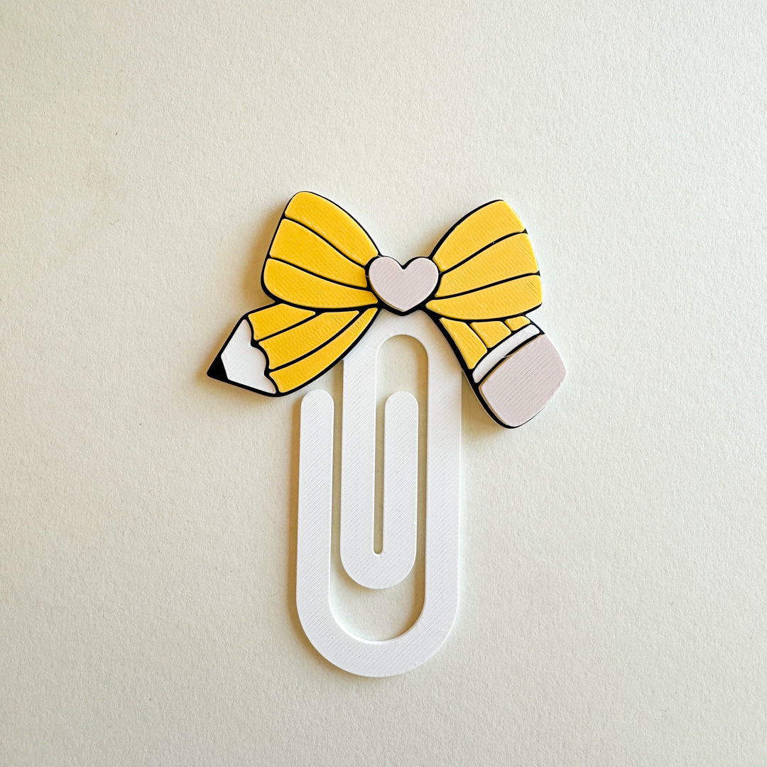 Pencil-shaped paper clip with yellow bow on a beige background